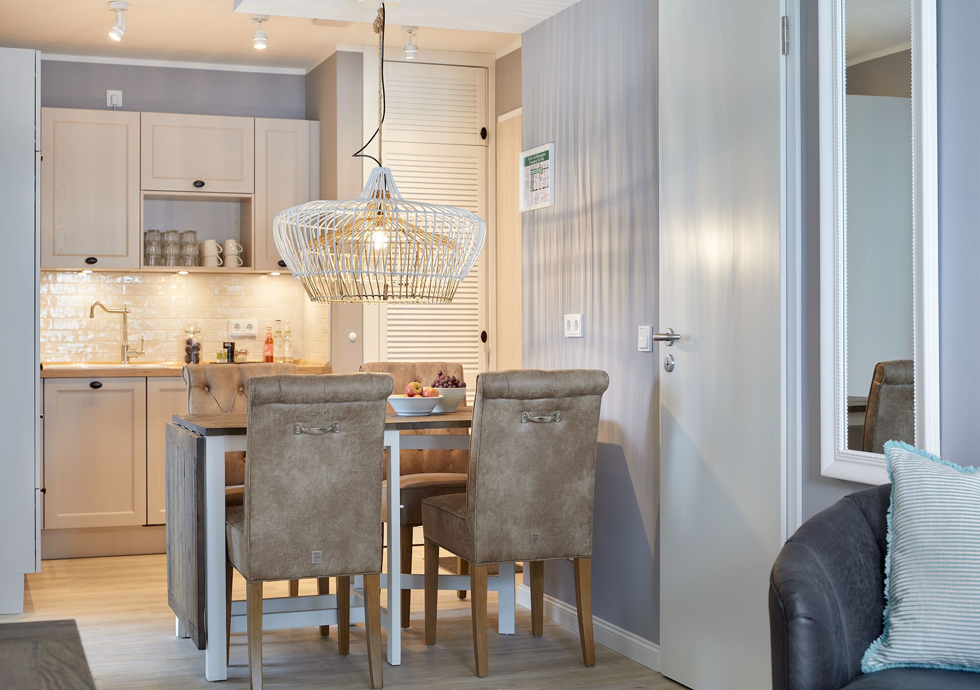 Une cuisine moderne avec un coin repas, comprenant un lustre, des meubles de couleur claire et une table à manger avec des chaises.