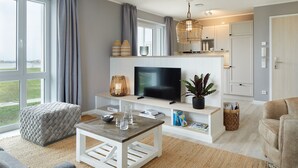 A modern living room with a TV, white furniture, a large window, and a view of the outdoors. - Beach Apartments Büsum (Büsum)