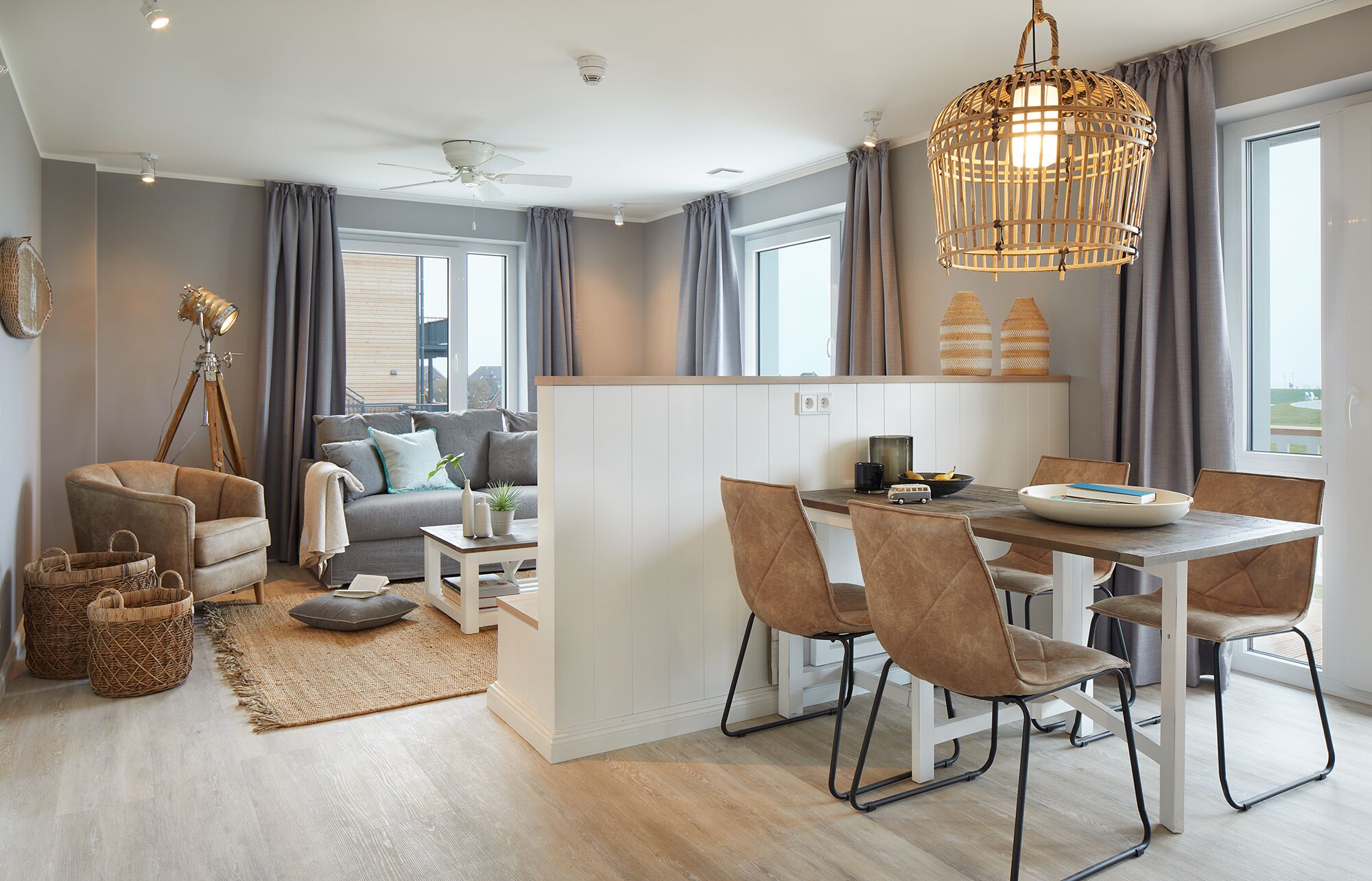 Een moderne woonkamer met een bank, een eettafel met stoelen, een compacte keukenhoek en een groot raam met gordijnen.