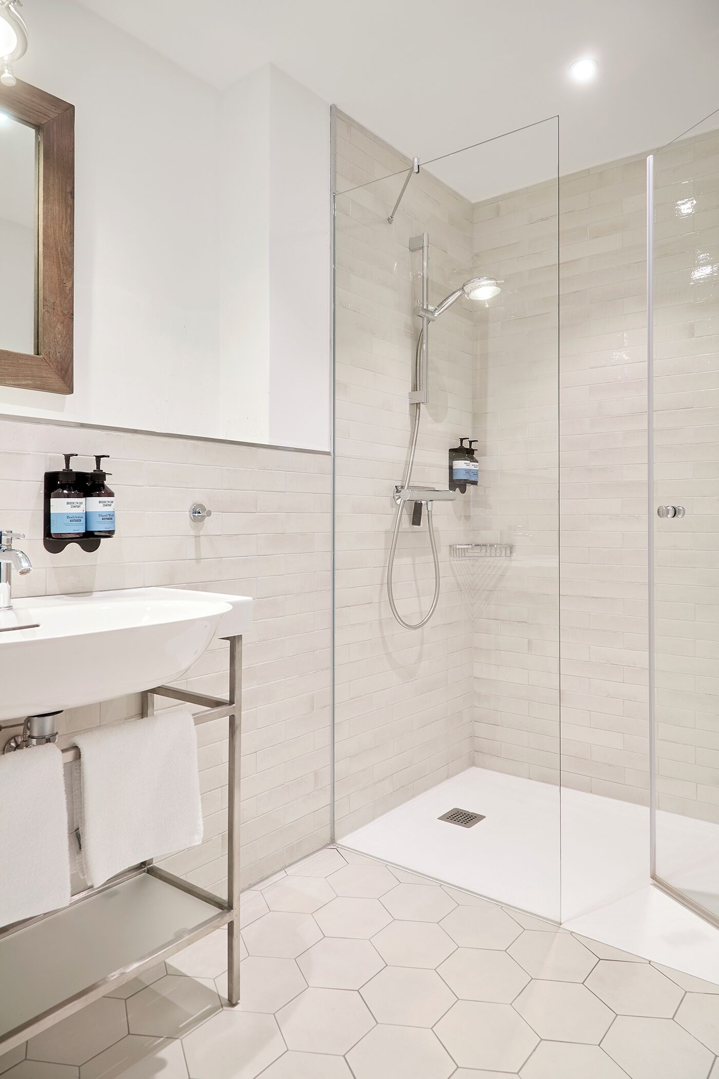 Un baño moderno con ducha envuelta en vidrio, un lavabo blanco con espejo y suelo de baldosas hexagonales.
