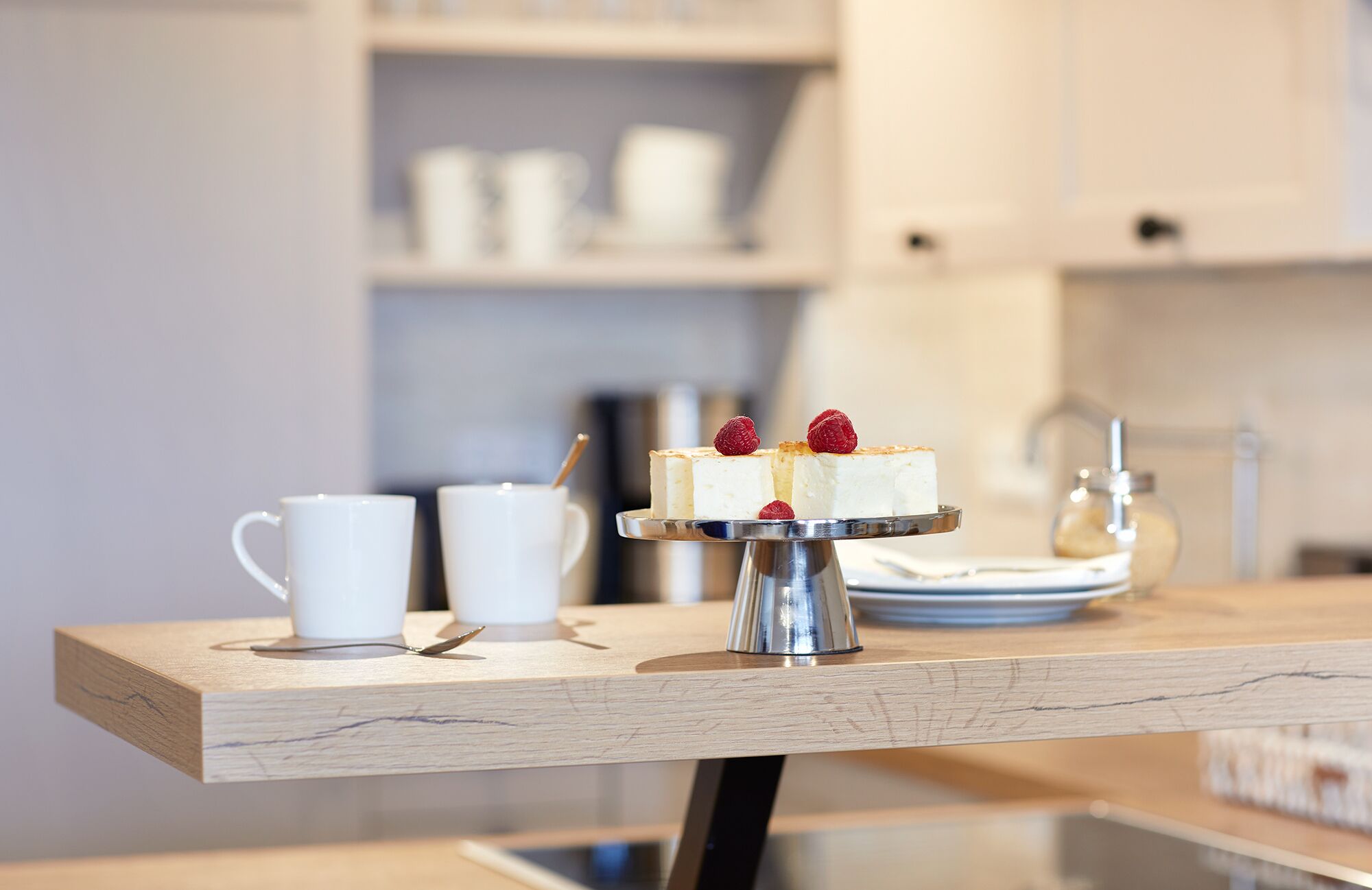 A dessert on a metal stand with a white cup and a spoon on a wooden table.