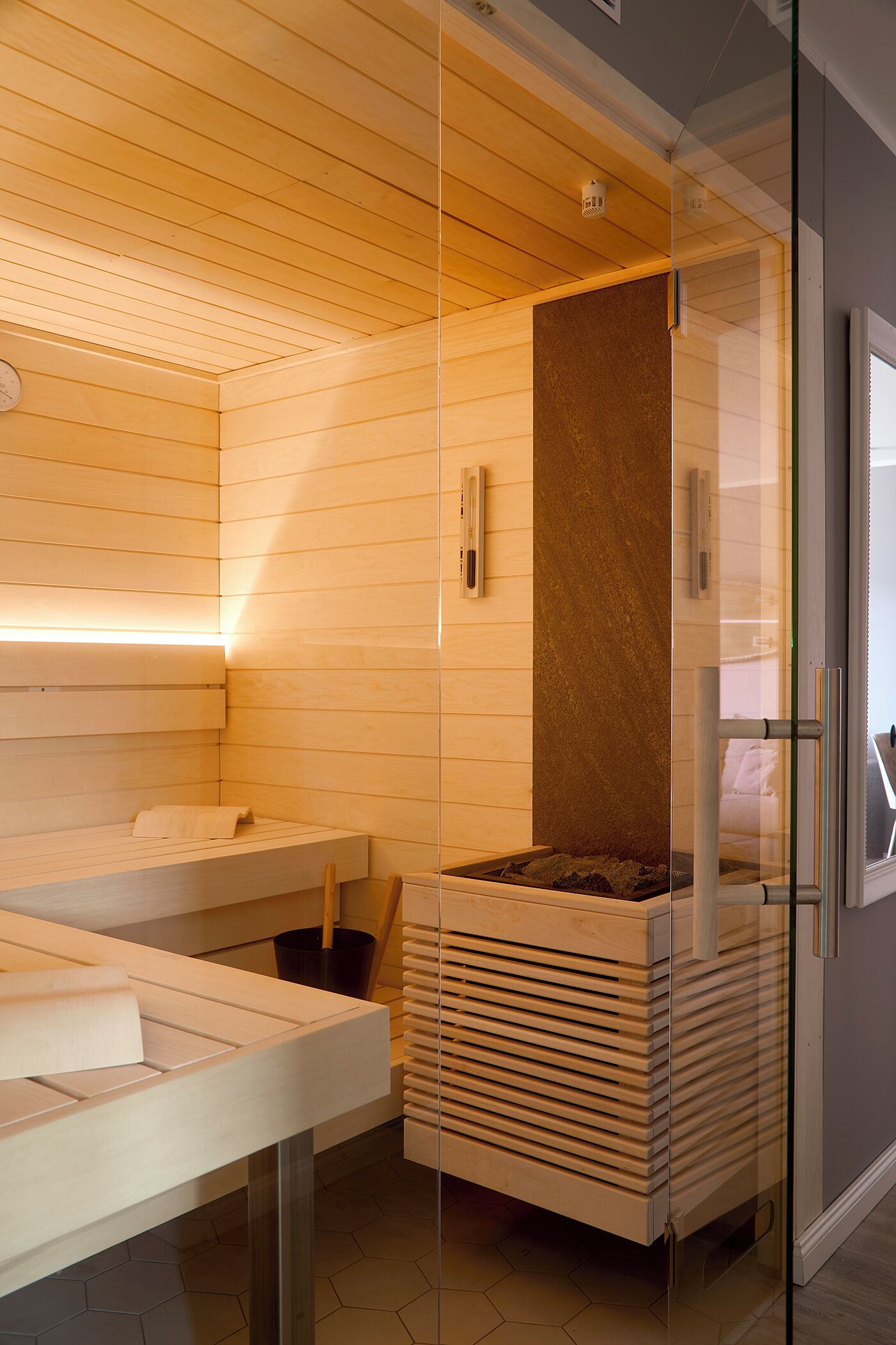 A sauna room with wooden benches, a glass partition, and a central heating element.