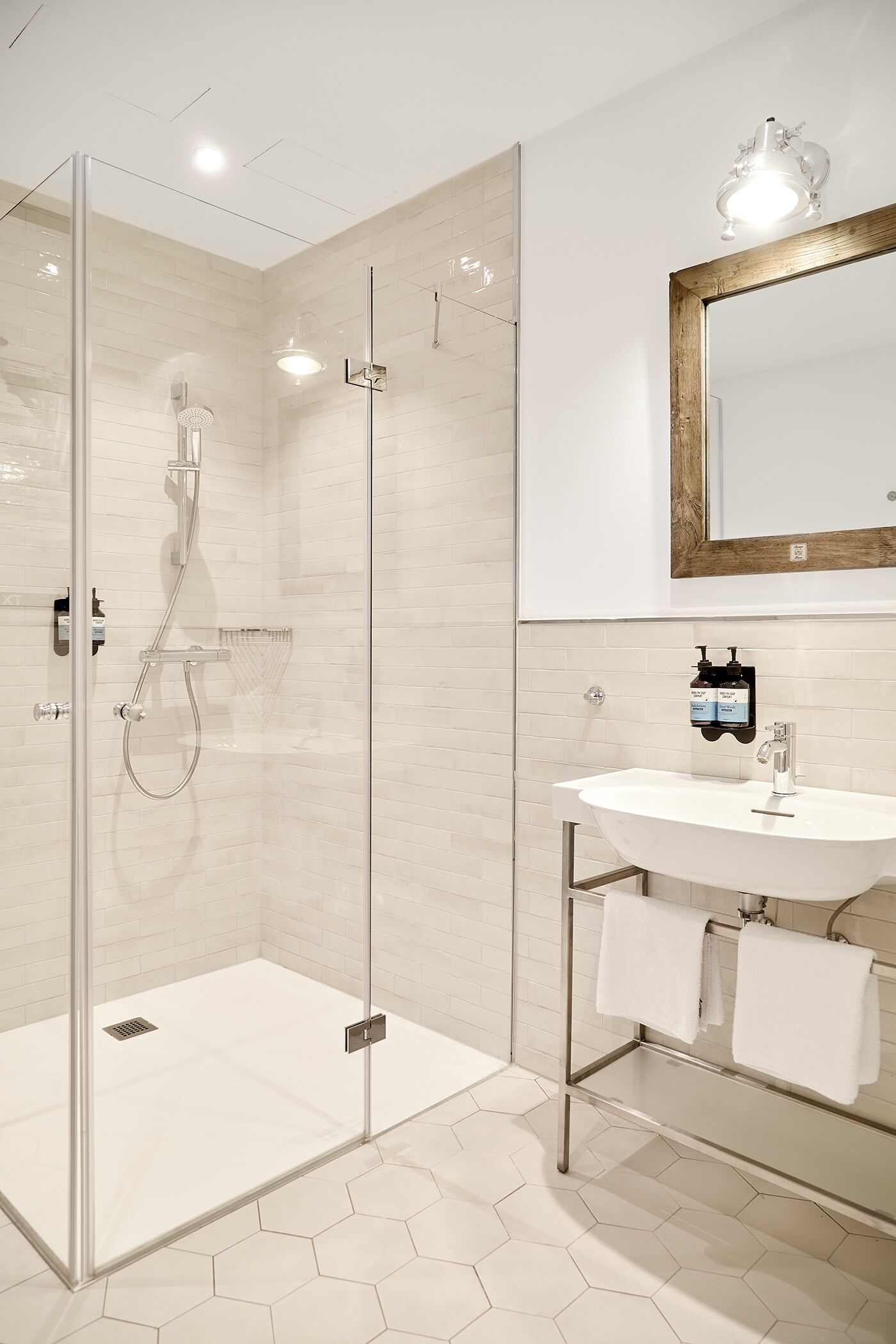 A modern bathroom with a glass-enclosed shower, a white sink with a mirror, and a hexagonal tile floor.