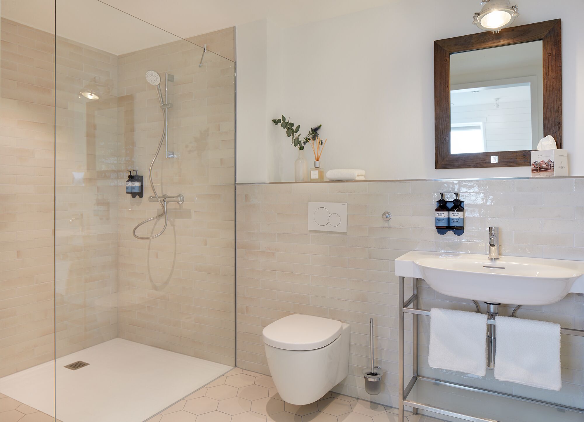 Une salle de bain moderne avec une douche à parois de verre, des toilettes blanches, un lavabo avec un miroir au-dessus et une petite plante accrochée au mur.