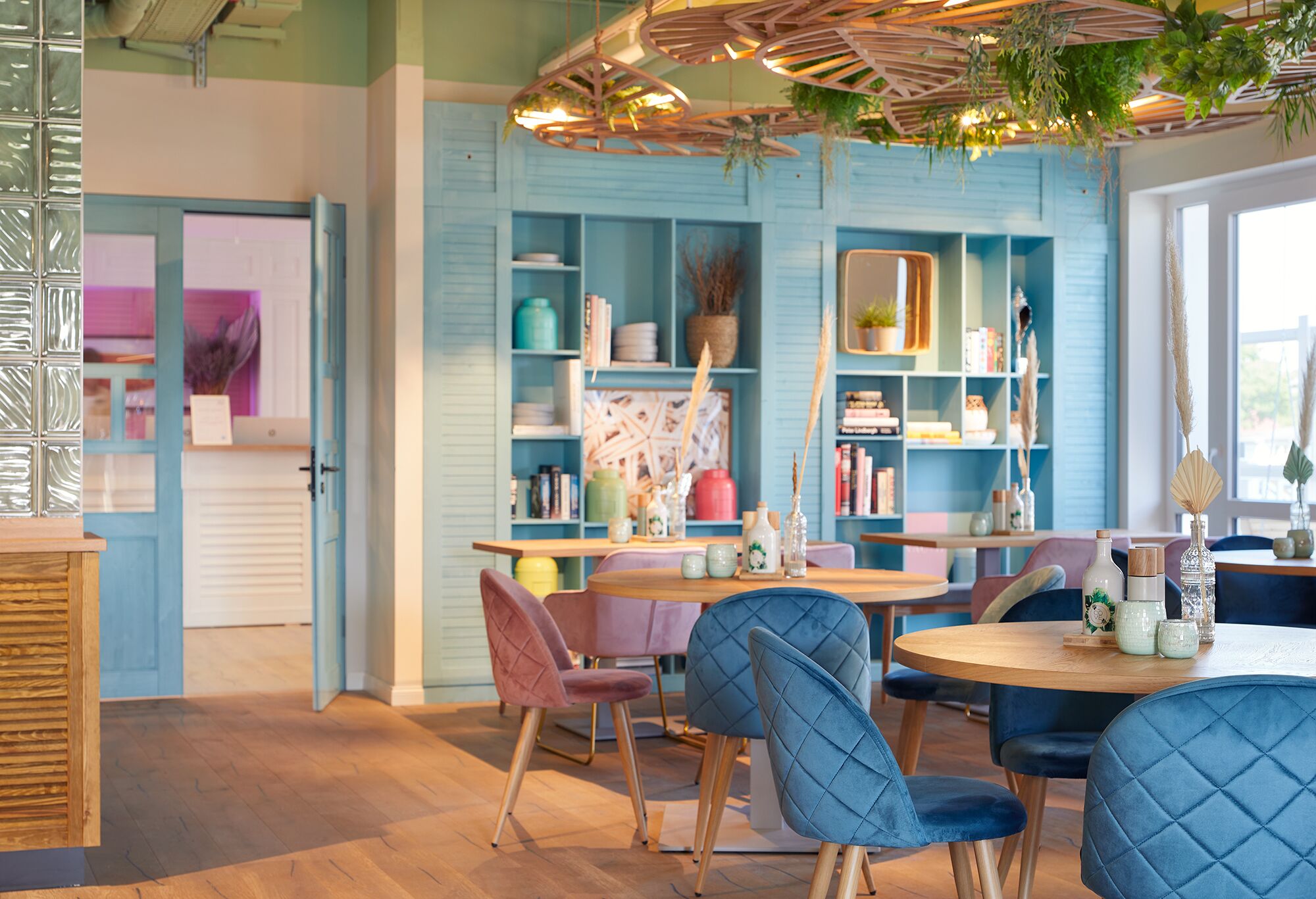 A cozy dining area with a wooden table and blue upholstered chairs, surrounded by shelves with various decorative items and books.