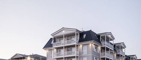 Un hotel de varios pisos con balcones, una zona exterior cubierta y un estacionamiento.
