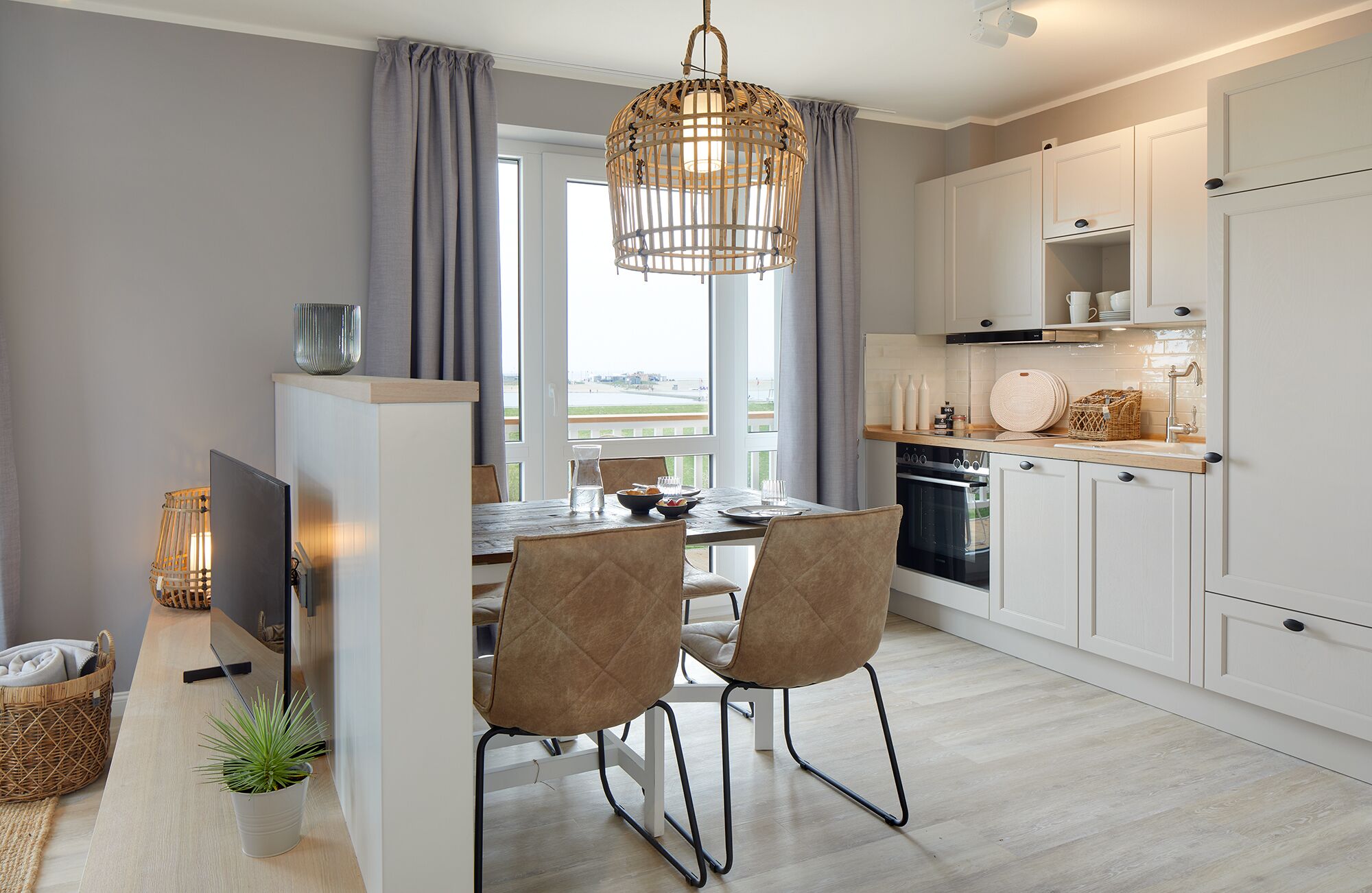 Een moderne keuken met witte kasten, een eethoek met een houten tafel en twee stoelen, en een groot raam met gordijnen.