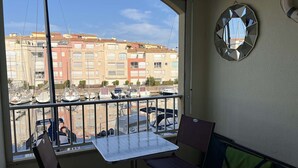 Un balcon avec une table et des chaises, donnant sur une marina où sont amarrés des bateaux et où se trouvent des immeubles d’habitation.