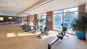 Un gimnasio con diversos equipos de ejercicio, amplias ventanas y suelo de madera.
