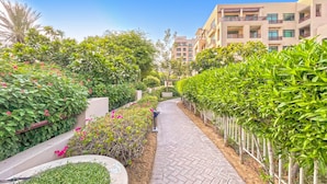 Un sendero bordeado de vegetación exuberante y plantas florecientes, que conduce a un edificio de varios pisos con balcones.