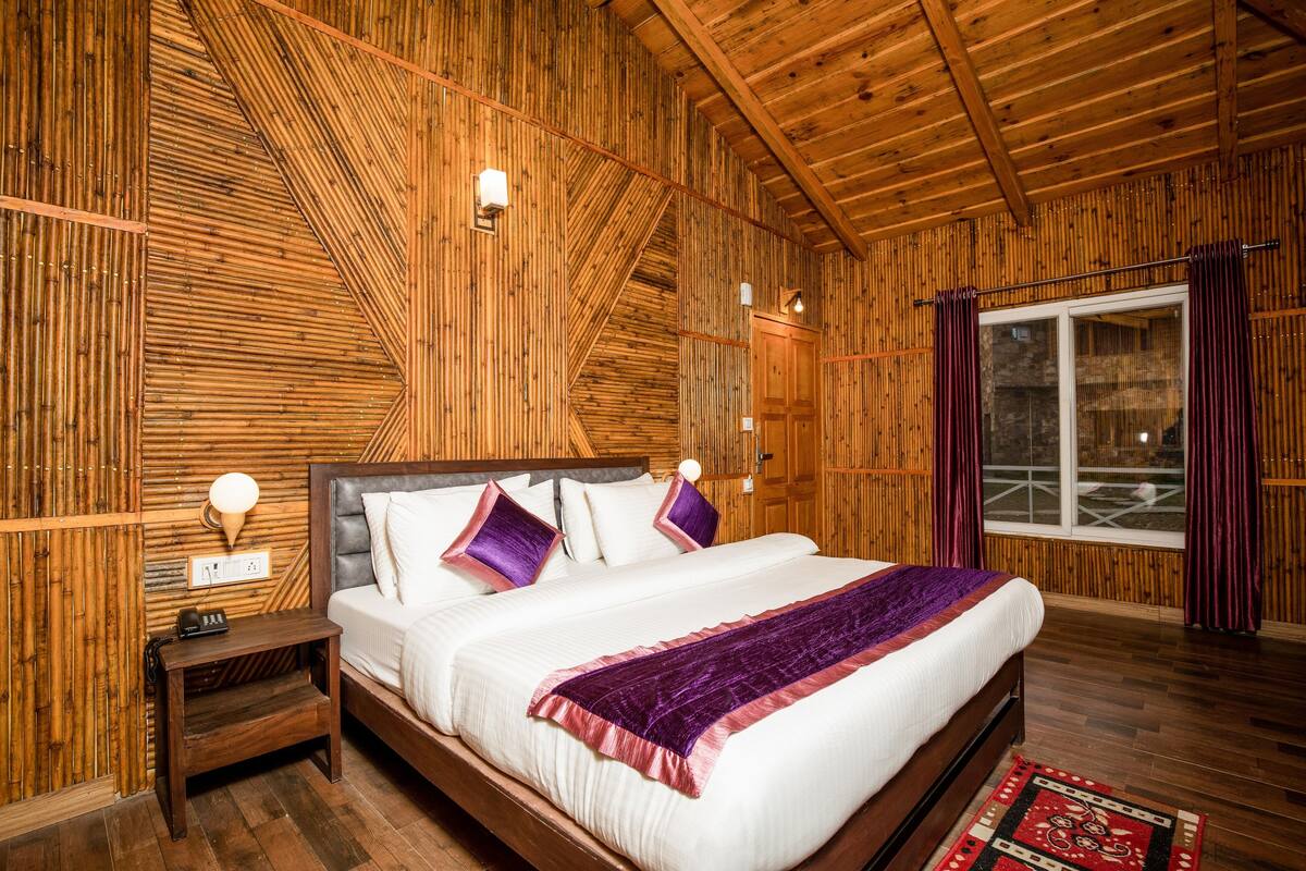 Una habitación con paneles de madera, una cama, una mesita de noche y una ventana con cortinas.