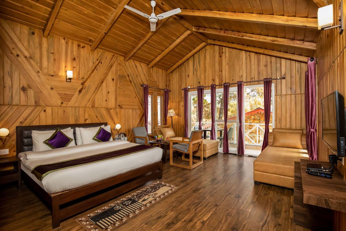 Interior de una cabaña de madera con cama, zona de estar y televisor.