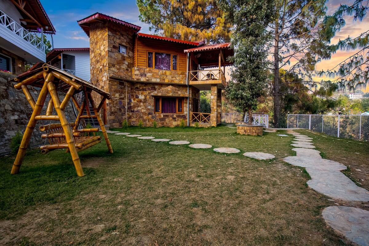 Una casa de piedra con un columpio de madera, un sendero de piedras y un balcón.