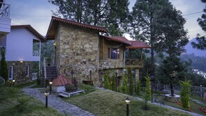 A stone building with a wooden deck and a red roof, surrounded by trees and a stone pathway.