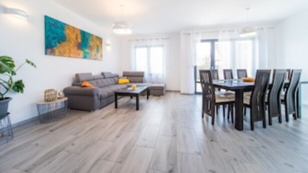 Una sala de estar moderna con un sofá gris, una mesa de centro y un comedor con mesa y sillas.