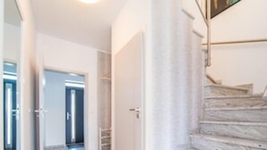 Un interior moderno con una escalera de madera, un pasillo que conduce a una puerta y un cuadro abstracto grande en la pared.