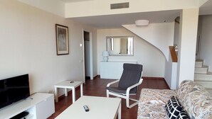 A living room with a TV, a white coffee table, a grey armchair, and a patterned sofa. - Spacious Duplex 300m from Beaches, Includes Parking (L'Ametlla de Mar)