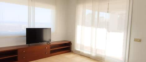 A living room with a TV on a wooden entertainment unit, a sofa, and a sliding glass door.
