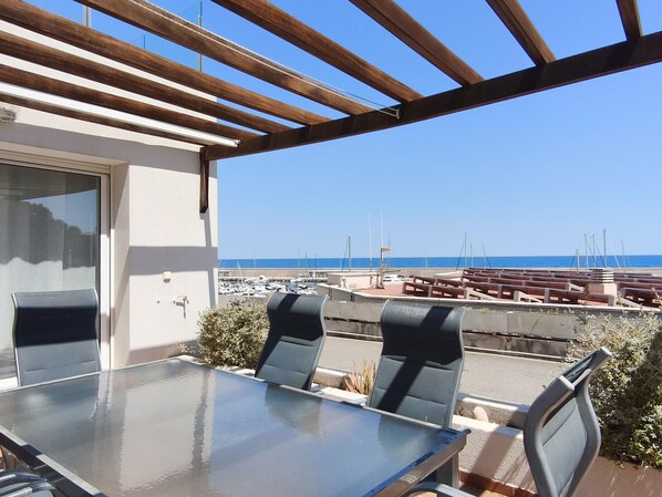 A balcony with a glass table and chairs, overlooking a marina and the sea. - Luxury Seafront Apartment for Families in L'Ametlla de Mar (L'Ametlla de Mar)