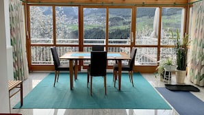 A dining area with a table and chairs, large windows with a view of a mountainous landscape, and potted plants. - Apartment with conservatory, wonderful panorama and large terrace (Landeck)