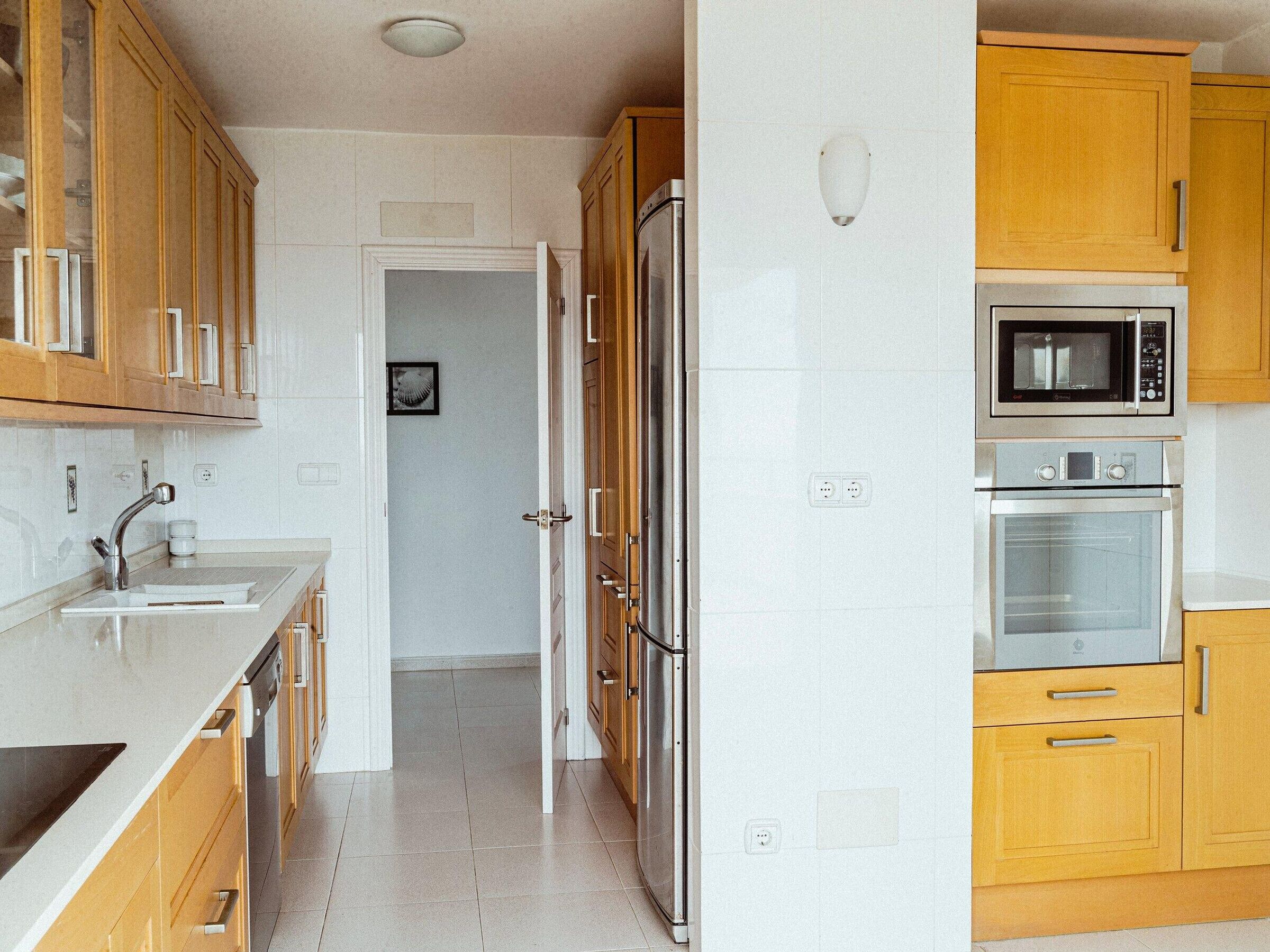 Een keuken met houten kastjes, een roestvrijstalen koelkast, een magnetron en een oven.