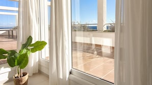 Ein Zimmer mit großem Fenster, weißen Vorhängen und einer Topfpflanze.