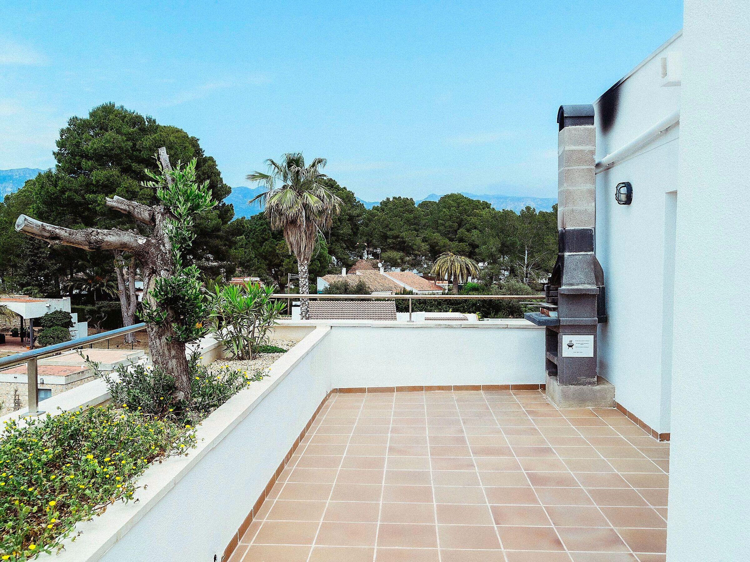 Une terrasse sur le toit, dotée d’un sol carrelé, d’un mur en pierre et offrant une vue sur un quartier résidentiel avec des arbres et des maisons.