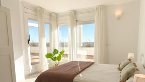 Ein Schlafzimmer mit einem großen Bett, weißen Vorhängen, einer Topfpflanze und Blick ins Freie.