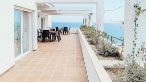 Eine moderne Terrassenanlage im Freien mit Meerblick, ausgestattet mit einem Tisch, Stühlen, einem gefliesten Boden und einem weißen Geländer.