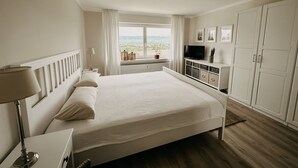 A bedroom with a large bed, a TV, a wardrobe, and a window with a view. - Romantic & stylish vacation apartment with two terraces and fantastic views (Höxter)