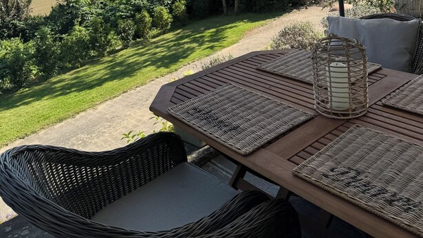 An outdoor patio with wicker furniture, a table with a woven placemat, and a large umbrella providing shade. - Romantic & stylish vacation apartment with two terraces and fantastic views (Höxter)