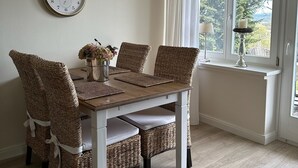 A dining area with a wooden table and wicker chairs, a wall clock, and a window with curtains. - Romantic & stylish vacation apartment with two terraces and fantastic views (Höxter)