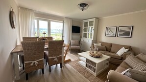 A spacious living room with a dining area, a sofa set, a television, and a view through the windows. - Romantic & stylish vacation apartment with two terraces and fantastic views (Höxter)