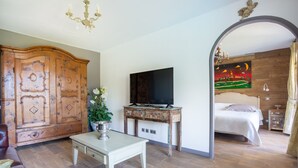 A room with a wooden cabinet, a television on a wooden stand, a bed with a white bedspread, and a chandelier. - Le Clos des Senteurs (Chateauneuf-Grasse)