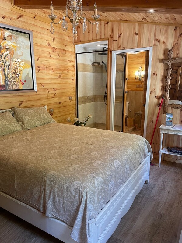 A wooden-paneled bedroom with a large bed, a shower, and a chandelier. - Le Clos des Senteurs (Chateauneuf-Grasse)