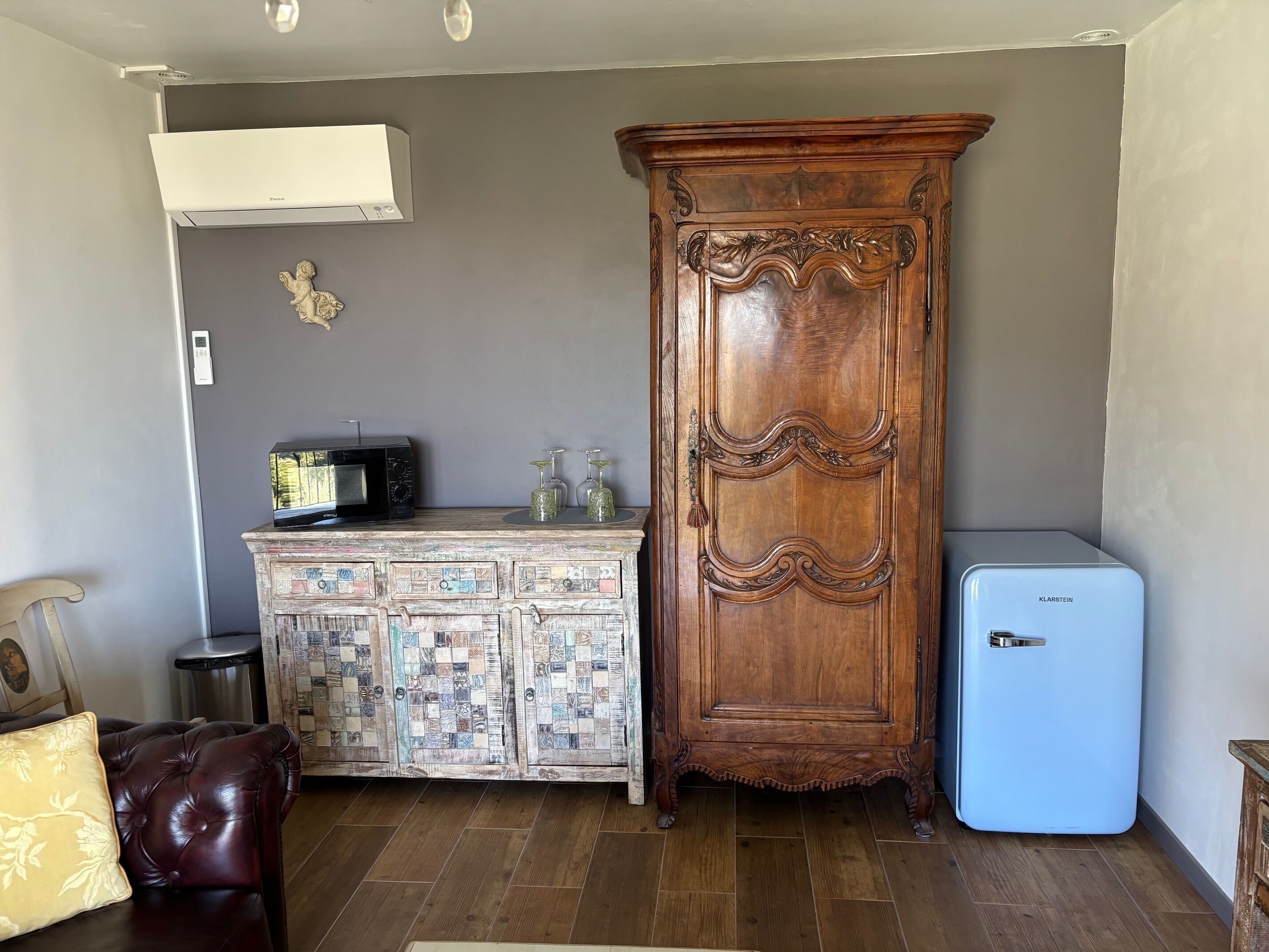 A compact living space with a wooden cabinet, a small refrigerator, a microwave, and a television on a wooden table.