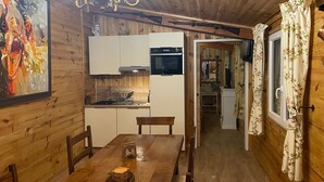 A wooden interior with a dining table, chairs, a chandelier, and a kitchen area. - Le Clos des Senteurs (Chateauneuf-Grasse)