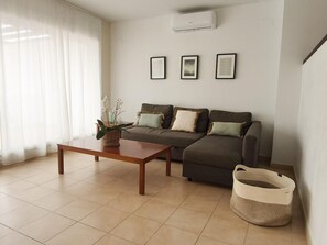 A living room with a sofa, a coffee table, and a wall-mounted air conditioner.