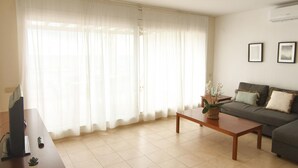 A living room with a sofa, a coffee table, a TV, and a plant. - Charming Apartment with Marina View in L'Ametlla de Mar (L'Ametlla de Mar)