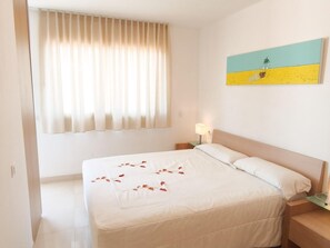 A hotel room with a bed, a nightstand, a lamp, a window with curtains, and a wall painting.