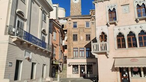A historic square with a prominent clock tower, traditional architecture, and a clear blue sky.