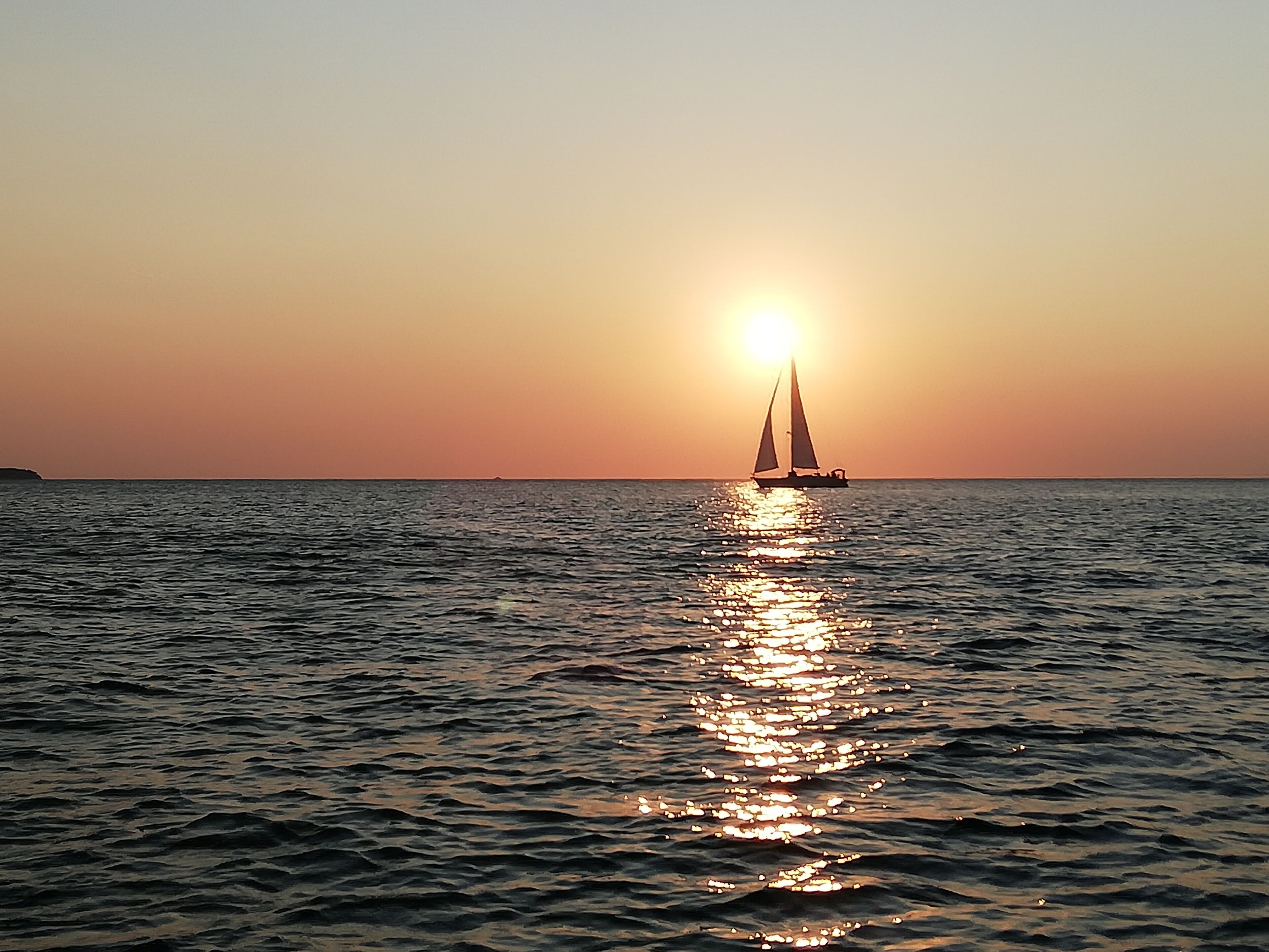 Un voilier sur une eau calme, avec un coucher de soleil en arrière-plan.