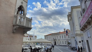 A historic square with ornate buildings, a covered seating area, and a clear sky.