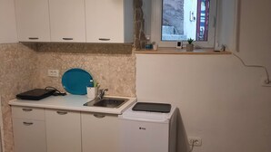 A compact kitchen with white cabinets, a blue cutting board, a sink, and a small window with a view of a stone wall.