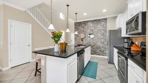 A kitchen with a central island, white cabinetry, a backsplash with a pattern, a stainless steel refrigerator, and a staircase leading to another level. - Modern Home, Private Pool. Sleeps 15 | WW102 (Kissimmee)