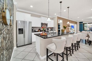 A modern kitchen with a central island, stainless steel appliances, white cabinetry, and bar stools. - Modern Home, Private Pool. Sleeps 15 | WW102 (Kissimmee)