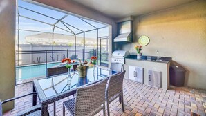 A balcony with a glass table, wicker chairs, a grill, and a view of a swimming pool. - Modern Home, Private Pool. Sleeps 15 | WW102 (Kissimmee)
