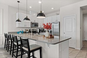 A modern kitchen with a central island, bar stools, a microwave, a refrigerator, and pendant lighting.