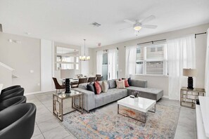 A modern living room with a gray sectional sofa, a glass coffee table, and a dining area with a white table and chairs.