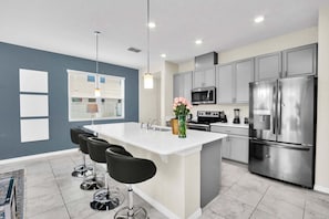 A modern kitchen with grey cabinets, stainless steel appliances, a central island with bar stools, and pendant lighting.